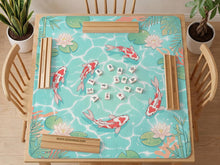 Turquoise square mahjong mat with koi fish, floating lily pads, pale lotus flowers, and green pond plants.