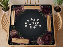 Black square mahjong mat with peony flowers in burgundy and soft pink, muted green leaves, and a blank center area.
