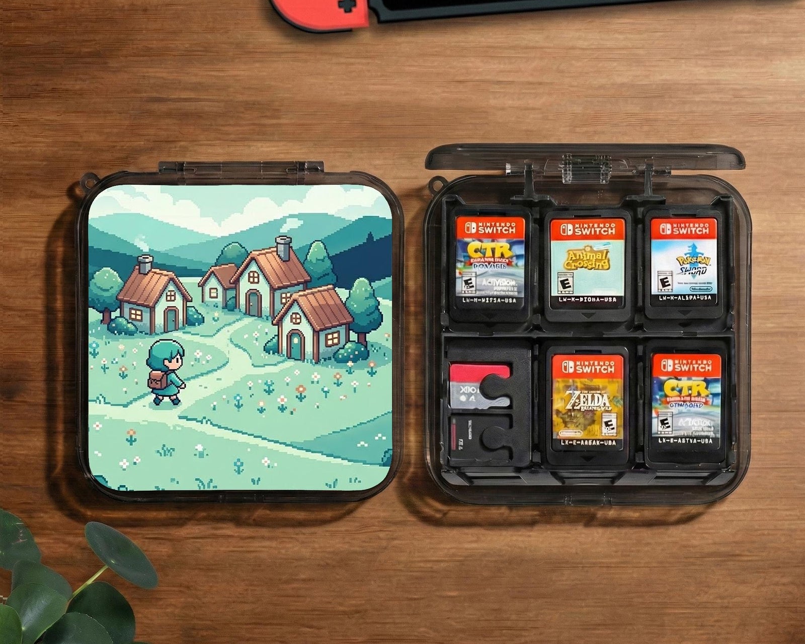 Teal carrying case with a pixel-style village scene, small houses, layered mountains, flowers, and a retro game-inspired landscape design.