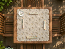 Neutral floral mahjong mat with delicate botanical line art and a scalloped edge on a cream background.