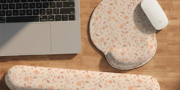 Blush pink floral mouse pad with wrist rest options, shown with peach blossoms, muted leaves, and a warm cream background.