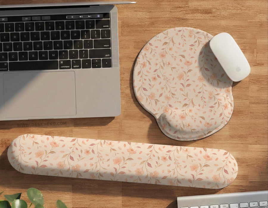 Blush pink floral mouse pad with wrist rest options, shown with peach blossoms, muted leaves, and a warm cream background.