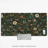 Floral butterfly desk mat in a dark green botanical print with cream and orange wildflowers, butterflies, moths and a bee, shown with a keyboard and mouse