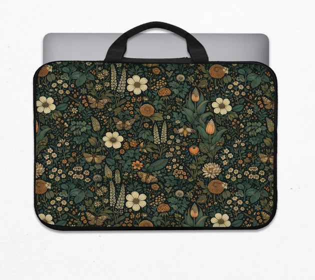 Padded cottagecore laptop sleeve with carry handles in a dark green botanical print with cream and orange wildflowers, butterflies and moths, holding a laptop
