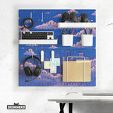 Anime pegboard wall organizer printed with a blue sky, pink clouds and a city skyline, holding a keyboard, game controller, headphones, pen cups and a folder on white shelves and hooks