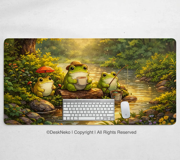 Forest frogs desk mat illustrated with three cute frogs by a sunlit forest stream, one with an umbrella, one drinking tea, and one fishing, shown with a keyboard and mouse