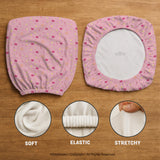 Pink chair cover with a pattern of moons, stars, bows, and small decorative shapes on a chair with armrests.