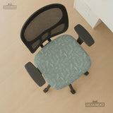 Office chair cover in muted sage green with a light leaf pattern on a white background.