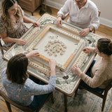 Square mahjong table mat with a cream center and a border design of cranes, bamboo, plum blossoms, and a geometric frame in sage green and warm gold.