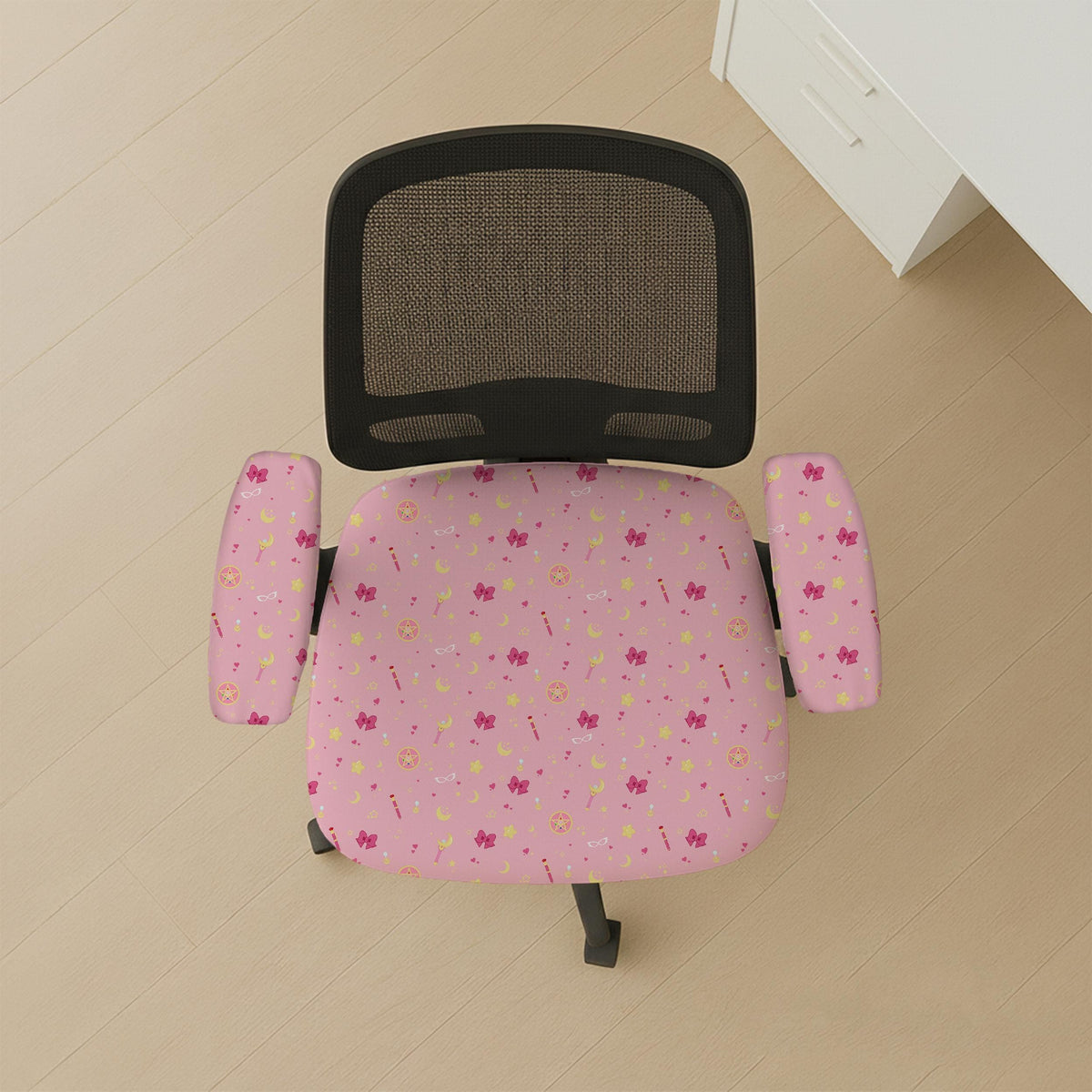 Pink chair cover with a pattern of moons, stars, bows, and small decorative shapes on a chair with armrests.