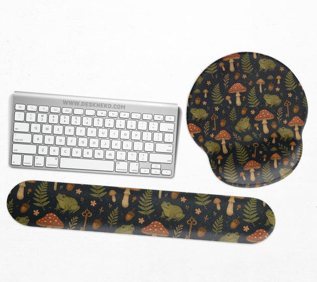 Dark botanical desk mat options with frogs, mushrooms, ferns, and acorns in brown and green tones, plus a matching keyboard wrist rest.