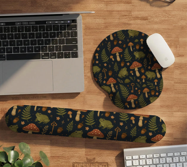 Dark botanical desk mat options with frogs, mushrooms, ferns, and acorns in brown and green tones, plus a matching keyboard wrist rest.