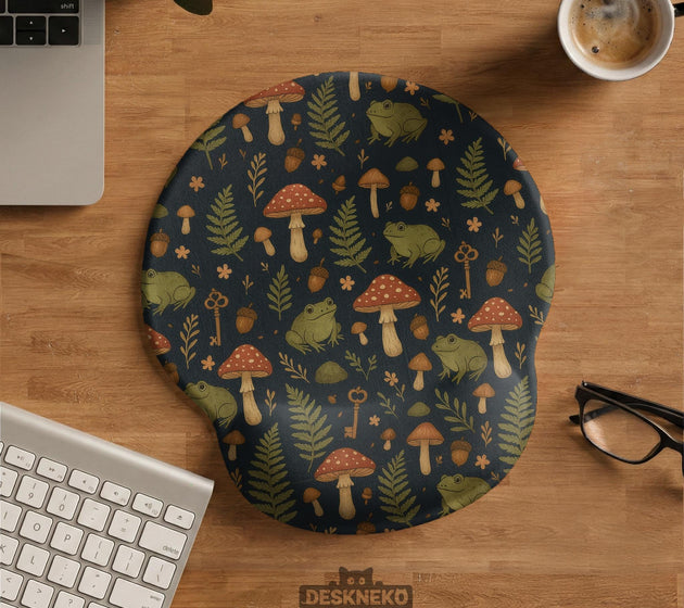 Dark botanical desk mat options with frogs, mushrooms, ferns, and acorns in brown and green tones, plus a matching keyboard wrist rest.