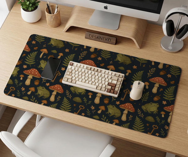 Dark forest-themed desk mat with an all-over pattern of frogs, mushrooms, fern leaves, acorns, tiny flowers, and antique keys.