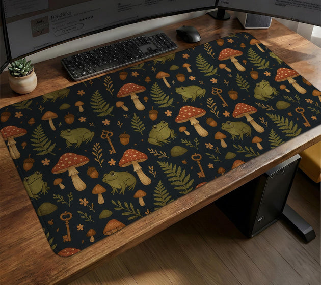 Dark forest-themed desk mat with an all-over pattern of frogs, mushrooms, fern leaves, acorns, tiny flowers, and antique keys.