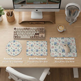 Floral desk mat with sage greenery, pink peonies, blue flowers, and a warm cream background.