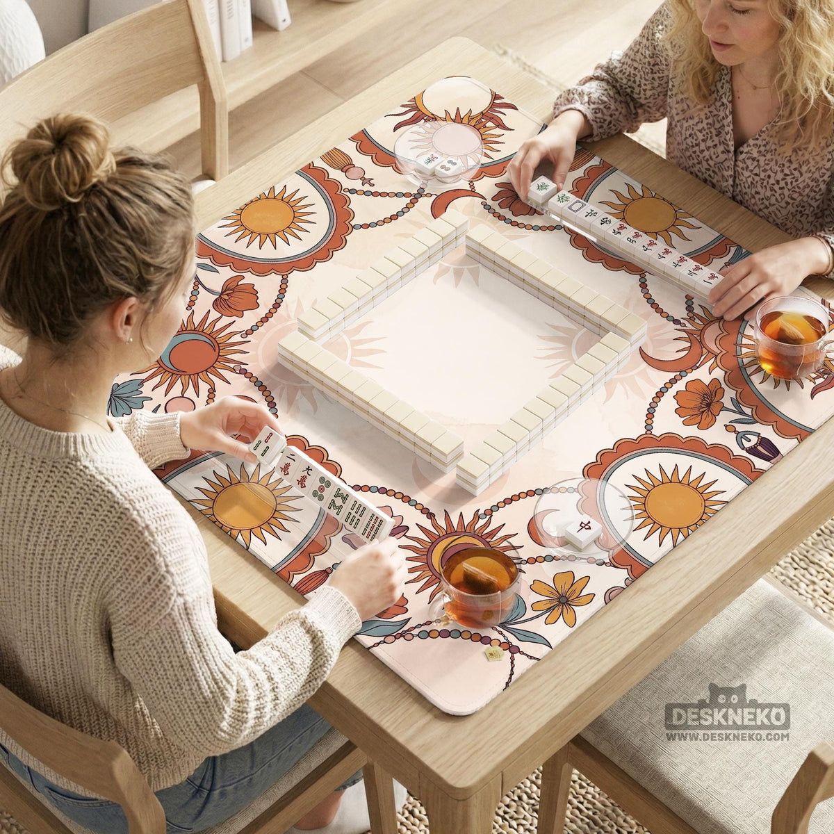 A square mahjong mat with a scalloped edge, sun and moon artwork, terracotta flowers, a soft cream background, and a decorative border around the play area.