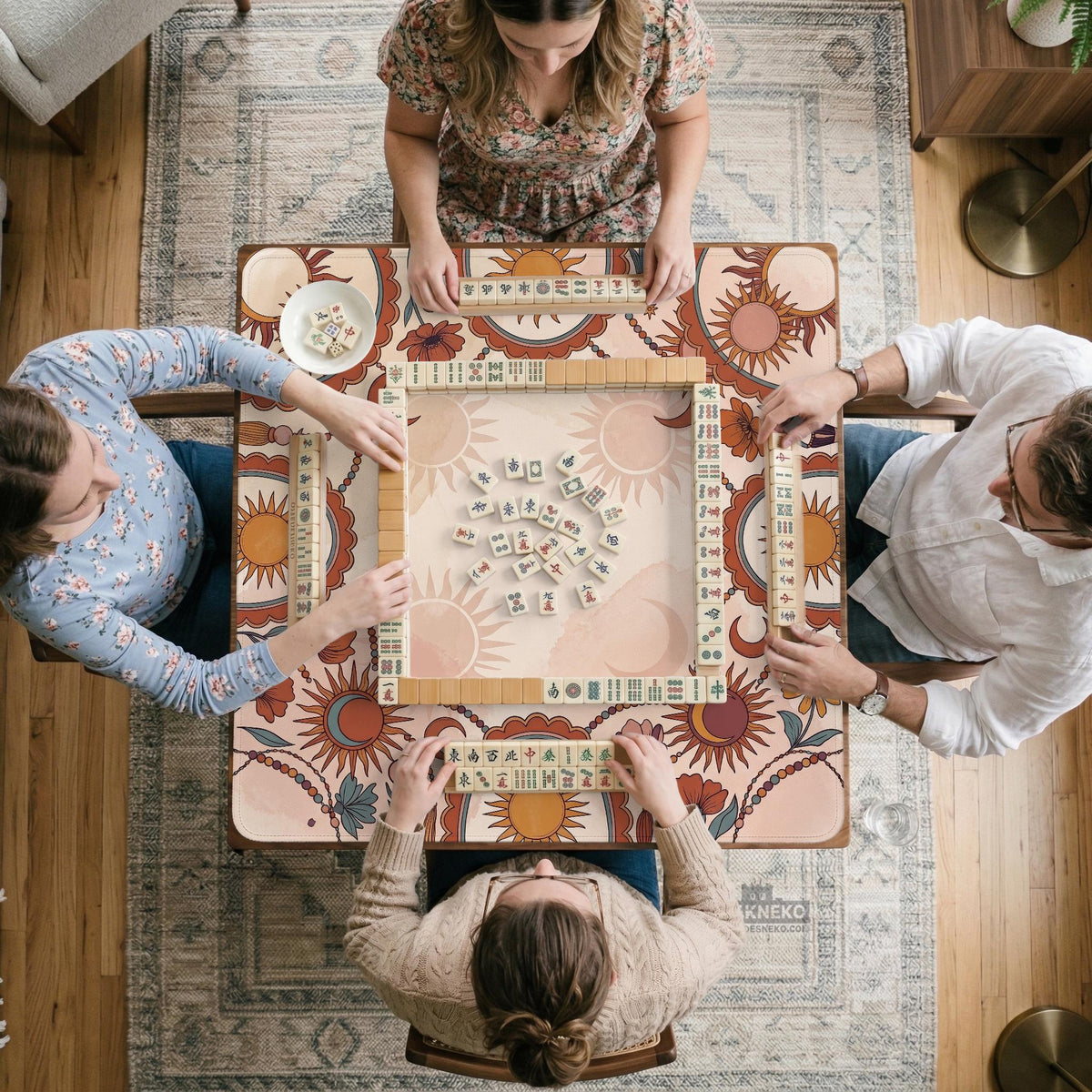 A square mahjong mat with a scalloped edge, sun and moon artwork, terracotta flowers, a soft cream background, and a decorative border around the play area.
