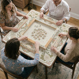 Square mahjong mat with a light floral border in sage green, cream, and blush around a plain center play area.