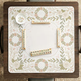 Square mahjong mat with a light floral border in sage green, cream, and blush around a plain center play area.
