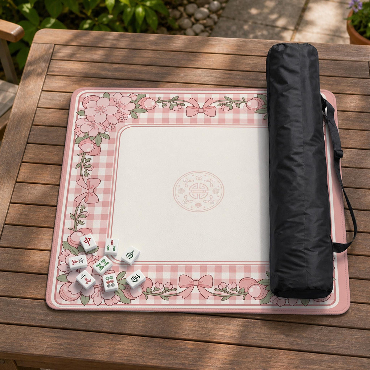 Square pink mahjong mat with a gingham border, floral corner details, and ribbon accents on a light background.