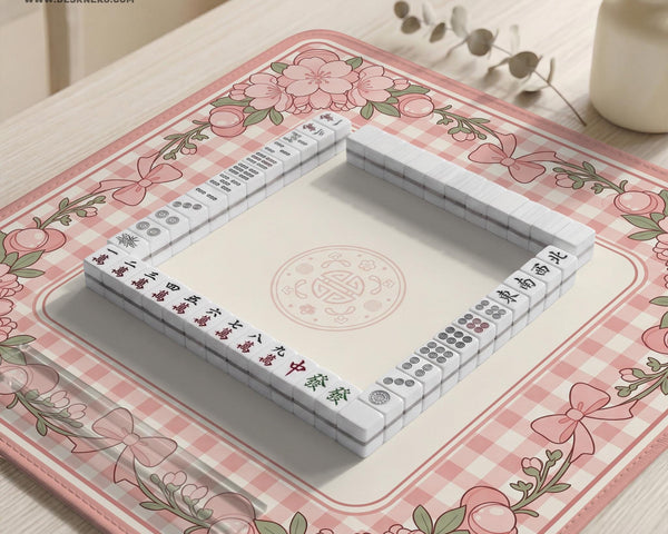 Pink gingham mahjong mat with a floral border, cherry blossom details, and a bow design around a plain center play area.