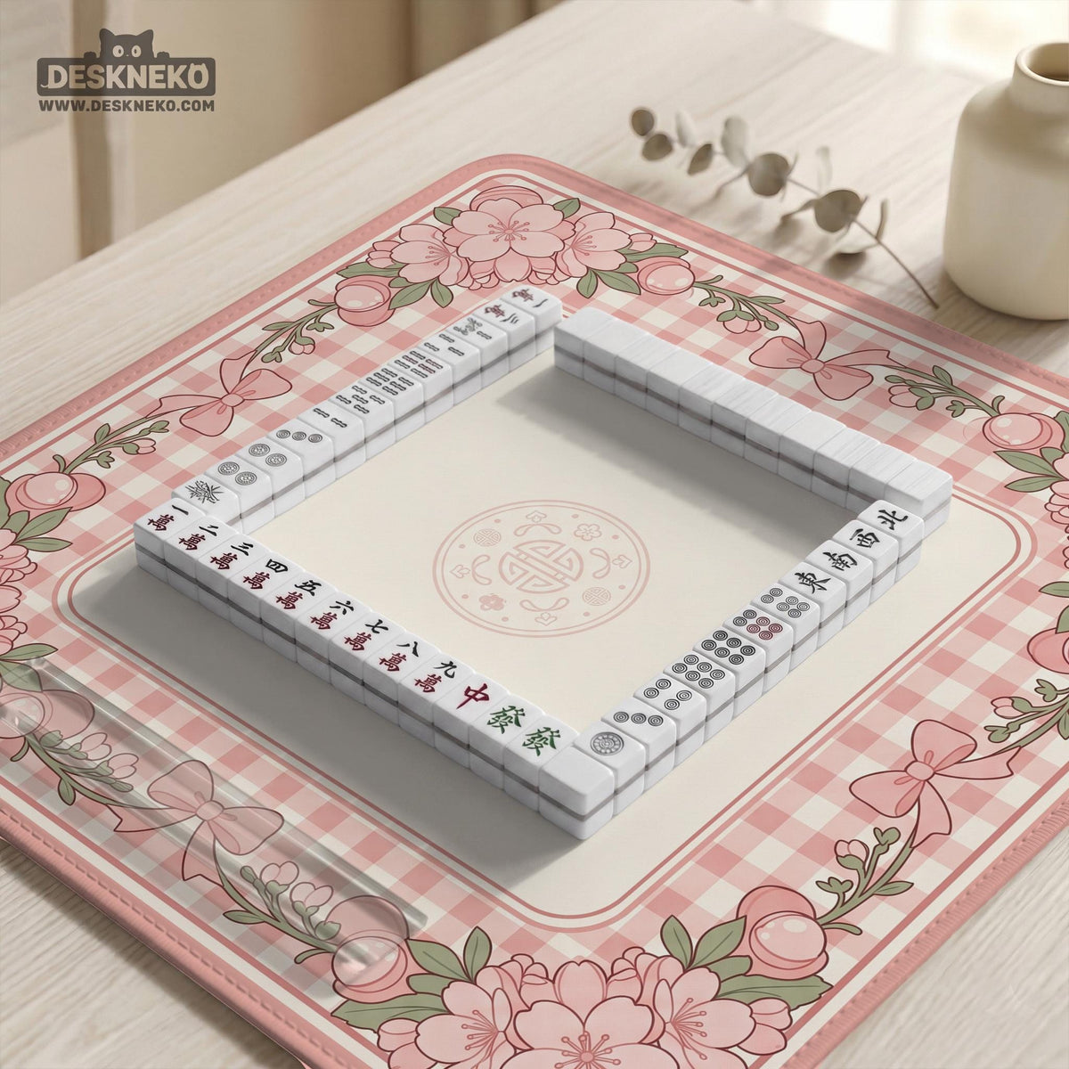 Square pink mahjong mat with a gingham border, floral corner details, and ribbon accents on a light background.