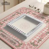 Square pink mahjong mat with a gingham border, floral corner details, and ribbon accents on a light background.