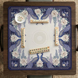 Blue mahjong table mat with a peacock and floral border, ivory center, lavender flowers, and scalloped edges.