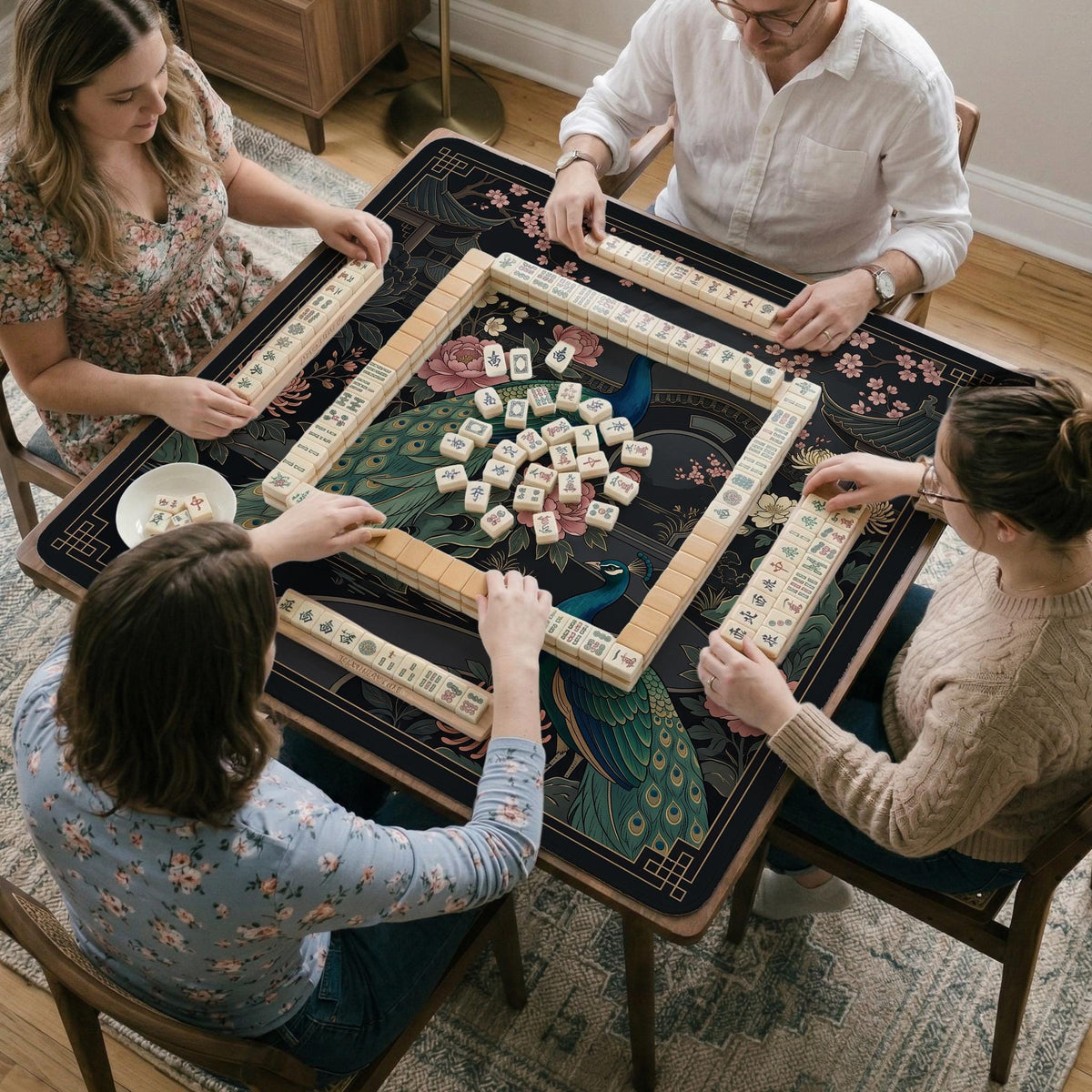 Square black mahjong mat with a gold peacock, blush flowers, and dark botanical artwork on a dark background.