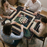 Square black mahjong mat with a gold peacock, blush flowers, and dark botanical artwork on a dark background.