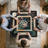 Square black mahjong mat with a gold peacock, blush flowers, and dark botanical artwork on a dark background.