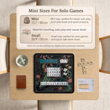 Square black mahjong mat with a gold peacock, blush flowers, and dark botanical artwork on a dark background.