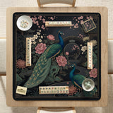 Square black mahjong mat with a gold peacock, blush flowers, and dark botanical artwork on a dark background.