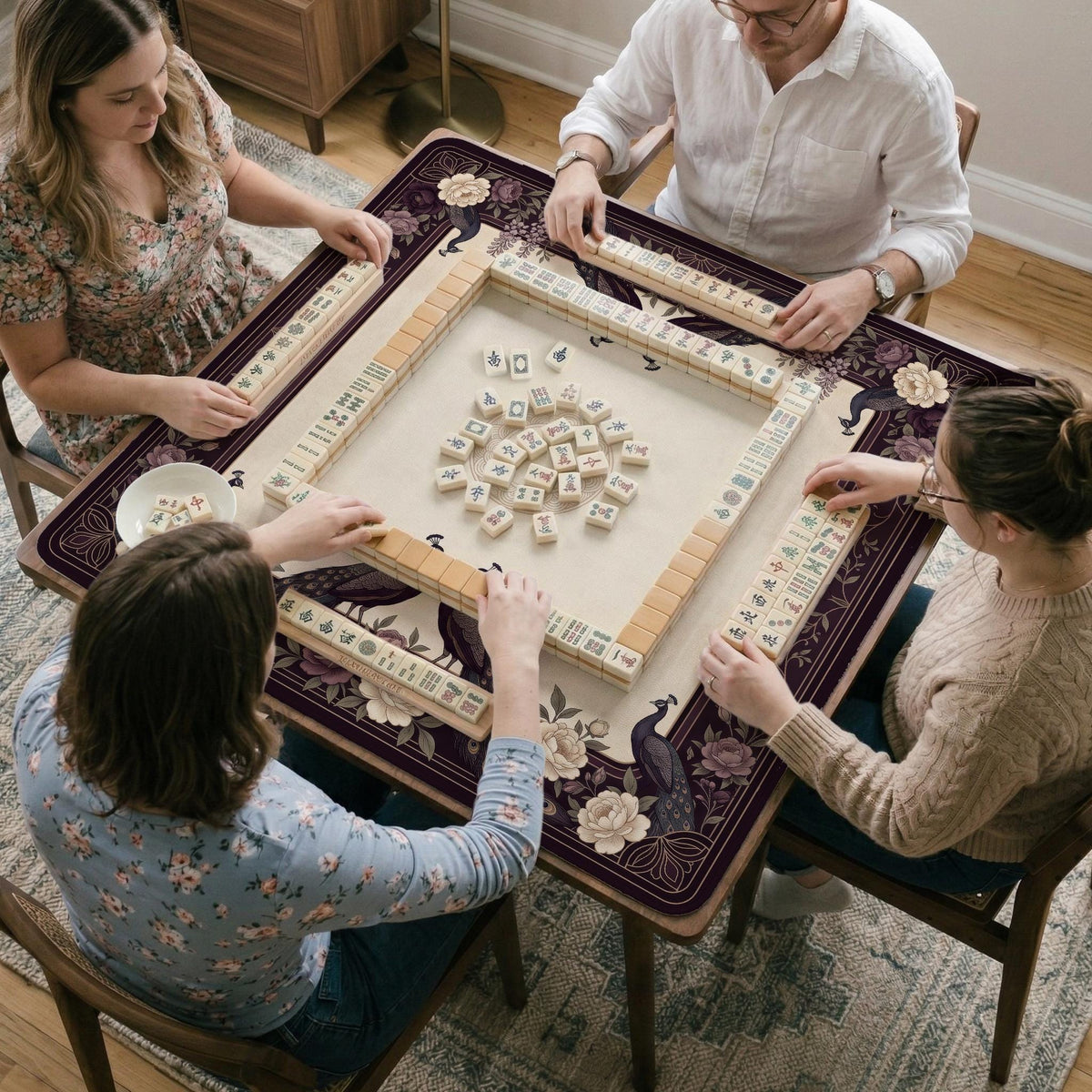 Square mahjong mat with a dark plum border, ivory floral pattern, muted sage leaves, and a decorative peacock garden design.