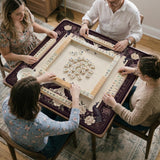Square mahjong mat with a dark plum border, ivory floral pattern, muted sage leaves, and a decorative peacock garden design.