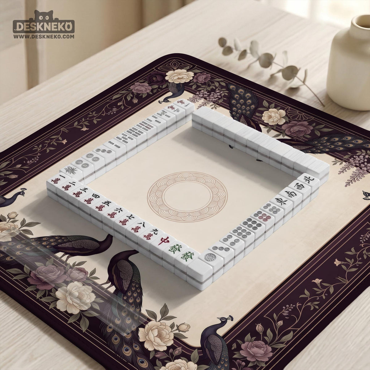 Square mahjong mat with a dark plum border, ivory floral pattern, muted sage leaves, and a decorative peacock garden design.