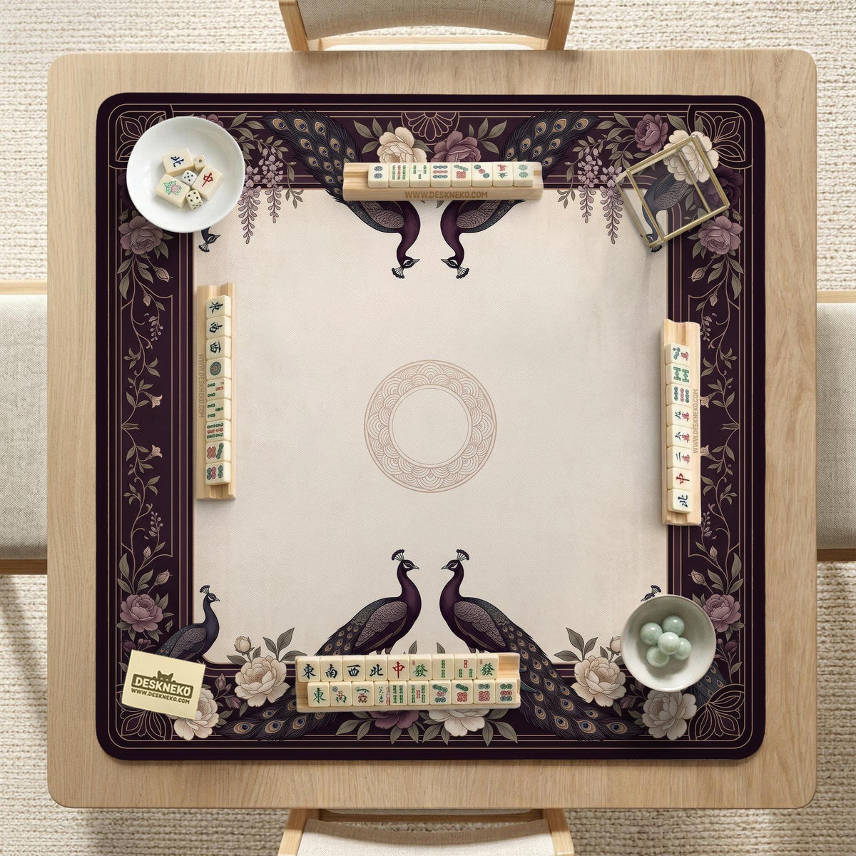Square mahjong mat with a dark plum border, ivory floral pattern, muted sage leaves, and a decorative peacock garden design.