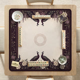Square mahjong mat with a dark plum border, ivory floral pattern, muted sage leaves, and a decorative peacock garden design.