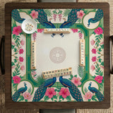 Green mahjong mat with peacocks, hibiscus flowers, tropical leaves, cream center space, and a scalloped floral border.
