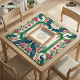 Green mahjong mat with peacocks, hibiscus flowers, tropical leaves, cream center space, and a scalloped floral border.