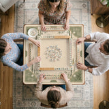 Square mahjong mat with a sage green bamboo and mountain design, cream center, scalloped border details, and gold line accents.