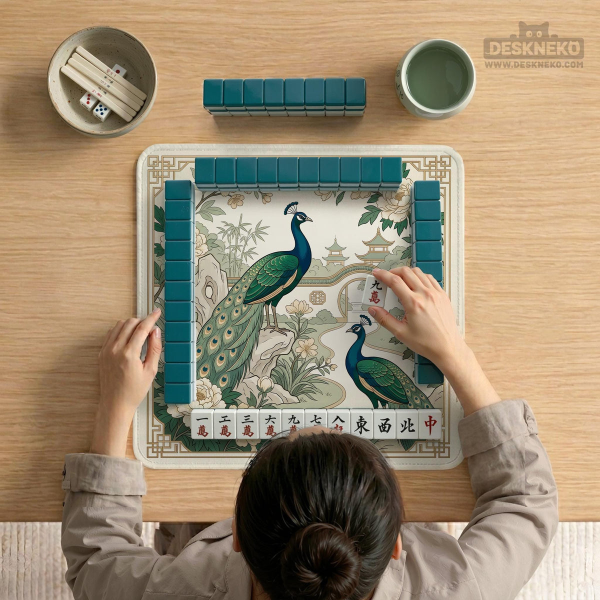 A green mahjong mat with peacock, floral, bamboo, pagoda, and gold border artwork in a scalloped chinoiserie style.