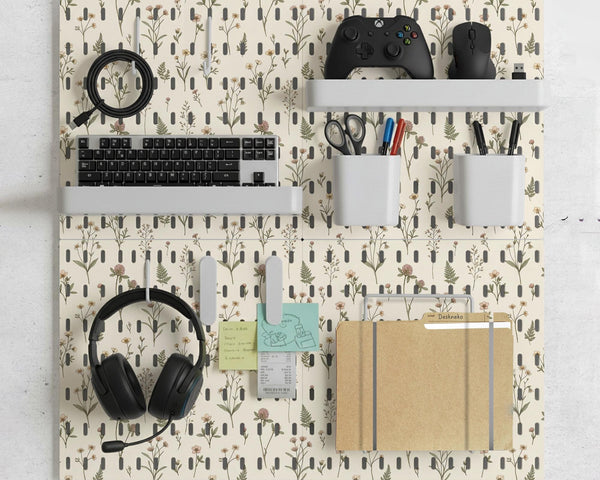 Cream pegboard wall organizer with small floral print, sage green stems, black slot layout, shelves, hooks, clips, and containers.