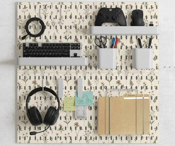 Cream pegboard wall organizer with small floral print, sage green stems, black slot layout, shelves, hooks, clips, and containers.