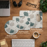 A desk mat with sage green abstract blocks, cream space, gray stone-like shapes, fine topographic contour lines, and small branch details.