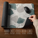 A desk mat with sage green abstract blocks, cream space, gray stone-like shapes, fine topographic contour lines, and small branch details.