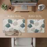 A desk mat with sage green abstract blocks, cream space, gray stone-like shapes, fine topographic contour lines, and small branch details.