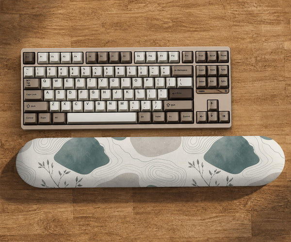 Sage green ergonomic mousepad and keyboard wrist rest with abstract shapes, soft gray details, cream space, topographic contour lines, and leafy branch accents.