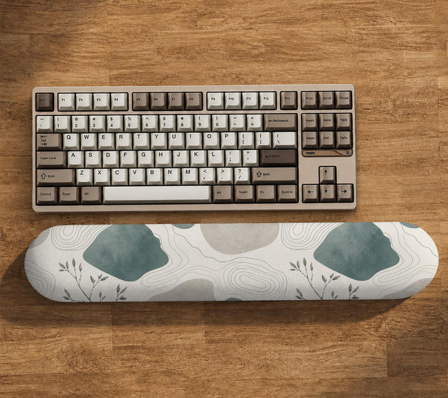 Sage green ergonomic mousepad and keyboard wrist rest with abstract shapes, soft gray details, cream space, topographic contour lines, and leafy branch accents.